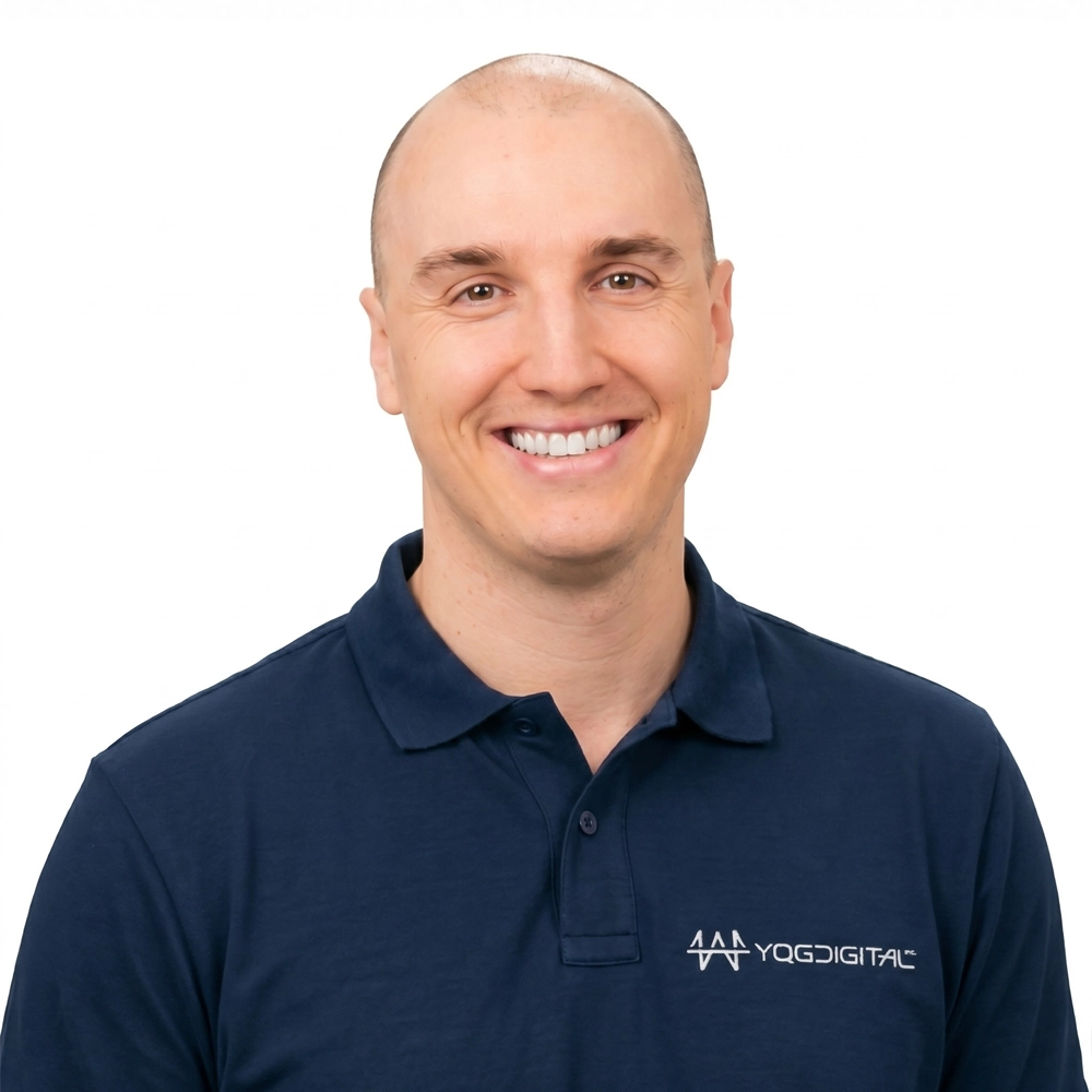 Portrait of a smiling man with a shaved head wearing a navy polo shirt with a white logo on the left chest against a white background.