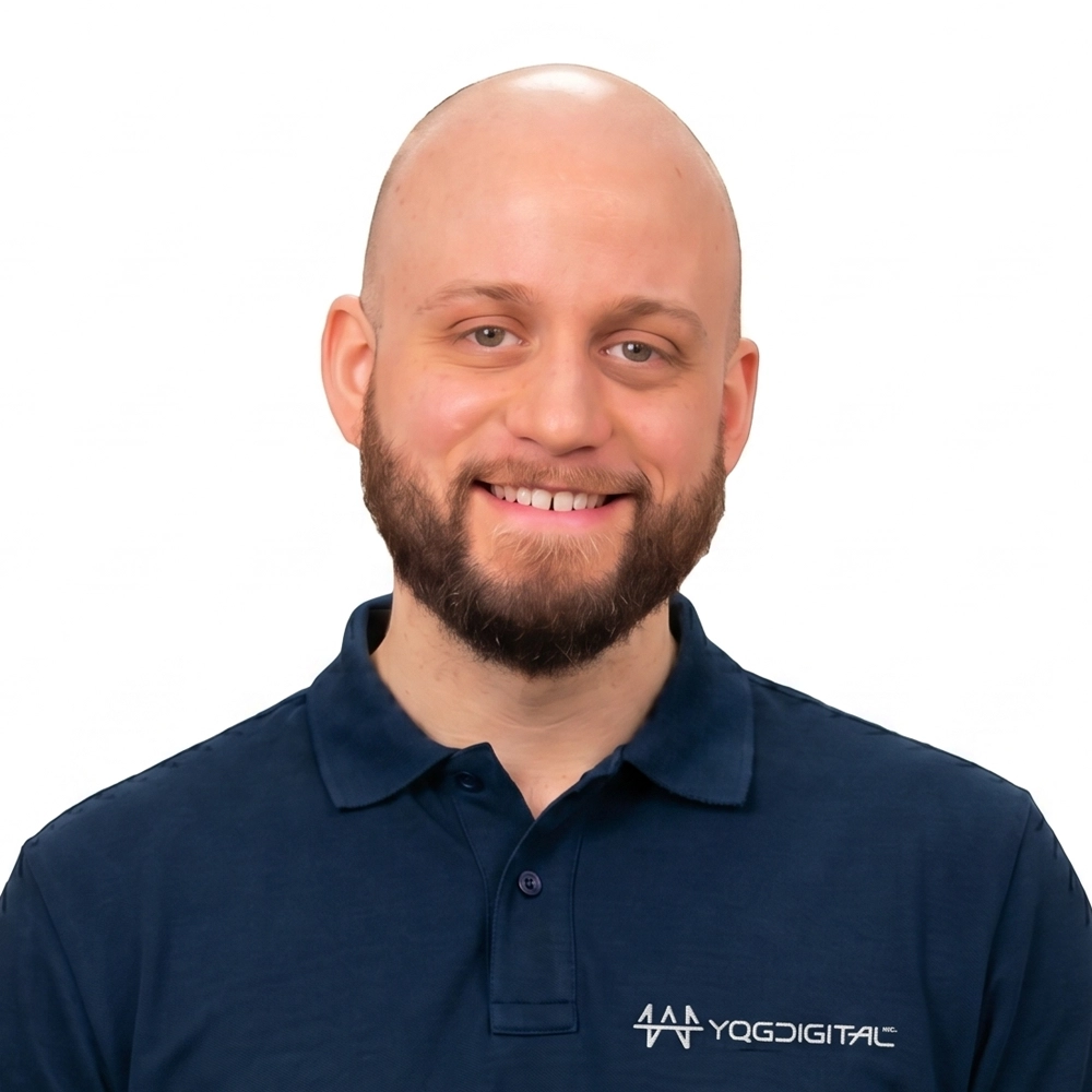 Smiling man with a beard and shaved head wearing a navy polo shirt on a white background.