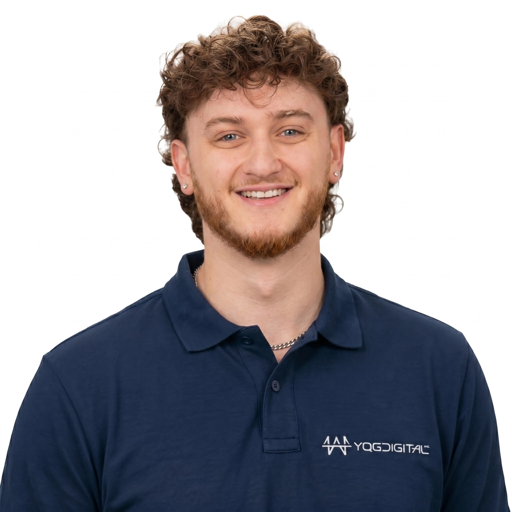 Smiling young man with curly brown hair and a light beard, wearing a navy polo shirt with a YQD Digital logo against a white background.